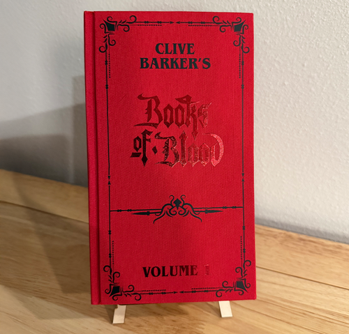 Red book titled 'Clive Barker's Books of Blood Volume 1' on a wooden surface with a white background