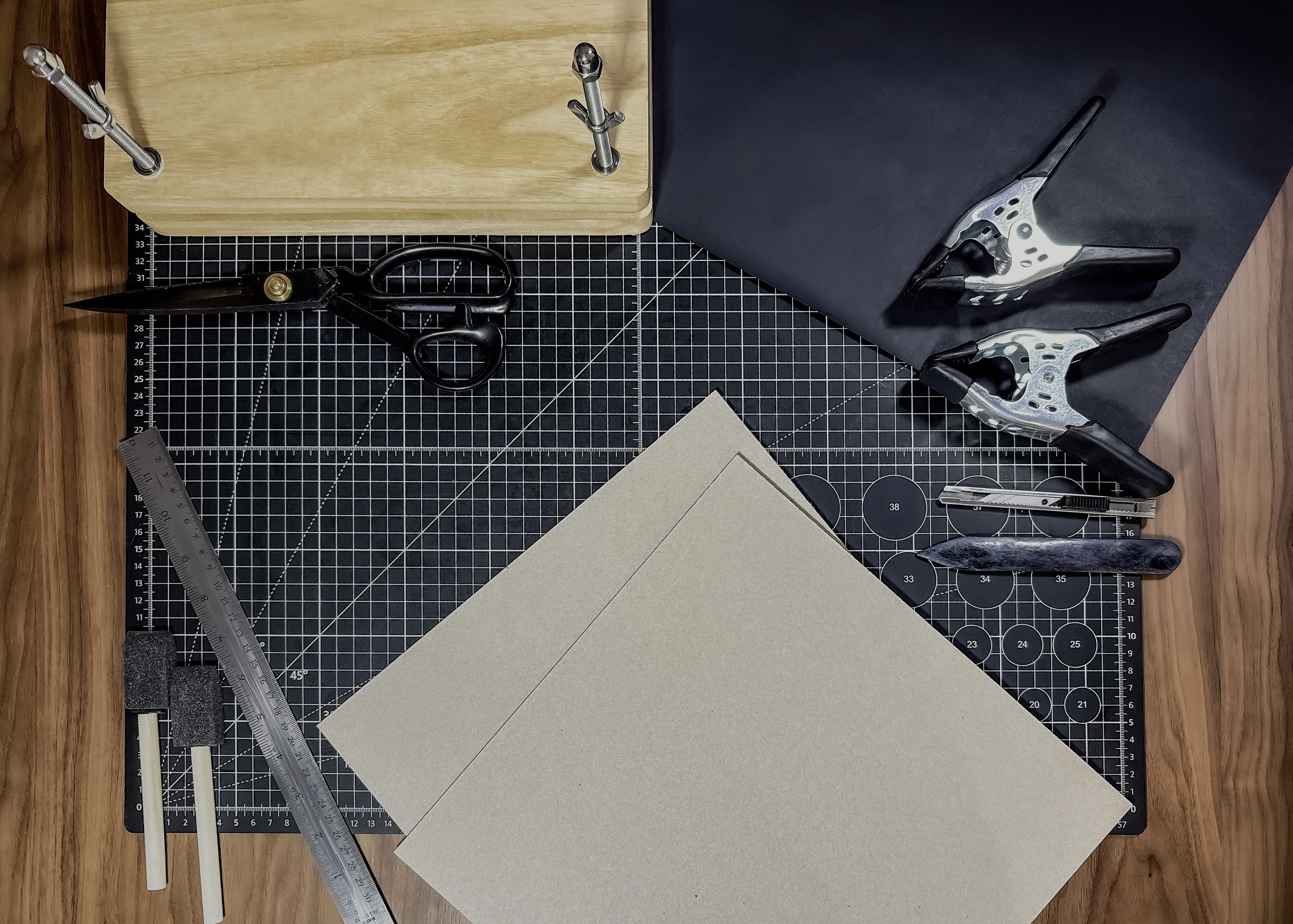 Crafting tools and materials on a cutting mat with a wooden surface.